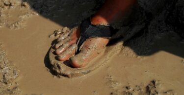 Imagem de um pé usando um chinelo, pisando na água e na lama suja.