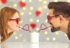Imagem de um casal jovem e feliz bebendo de canudinho de coração uma bebida em uma xícara branca, trazendo o conceito de sentimentos de puro carinho e amor.