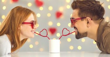 Imagem de um casal jovem e feliz bebendo de canudinho de coração uma bebida em uma xícara branca, trazendo o conceito de sentimentos de puro carinho e amor.
