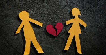 Imagem de um casal desenhando em papel e ao centro a foto de um coração partido, simbolizando o fim do amor.