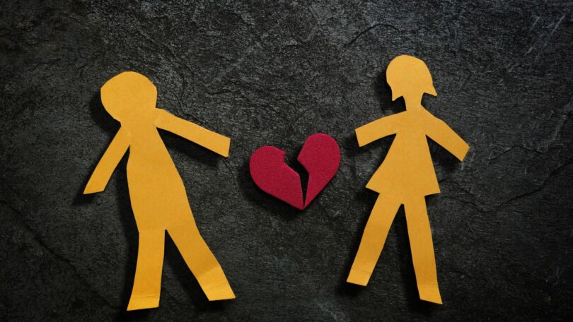 Imagem de um casal desenhando em papel e ao centro a foto de um coração partido, simbolizando o fim do amor.