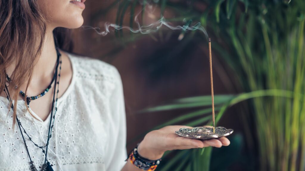 Imagem de uma mulher, segurando um bastão de incenso,  fazendo uma limpeza de cura espiritual e renovação emocional.
