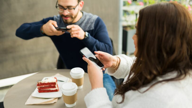 Imagem de dois criadores de conteúdo postando fotos de seu café nas redes sociais.