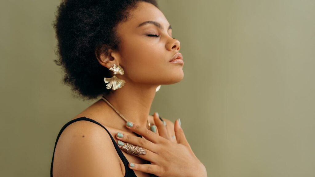 Imagem de uma mulher com blusa preta de alça fina, fazendo uma meditação e um acolhimento interior para sua evolução espiritual.
