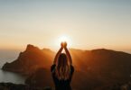 Imagem de uma jovem em pose espiritual segurando a luz do sol sobre as montanhas.