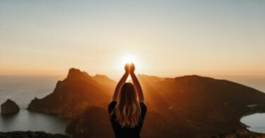 Imagem de uma jovem em pose espiritual segurando a luz do sol sobre as montanhas.