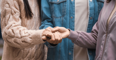 As mãos de duas mulheres e um homem estão no centro da imagem. Eles unem as suas mãos umas com as outras.