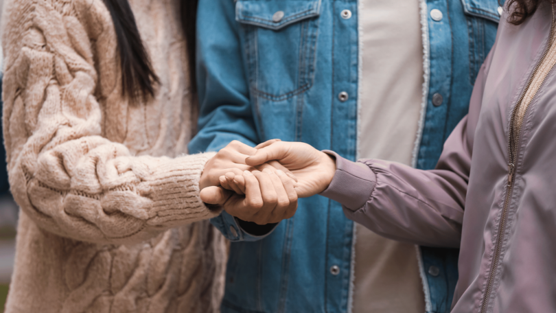 As mãos de duas mulheres e um homem estão no centro da imagem. Eles unem as suas mãos umas com as outras.