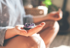 Uma mulher sentada está meditando com um cristal de quartzo na sua mão direita.