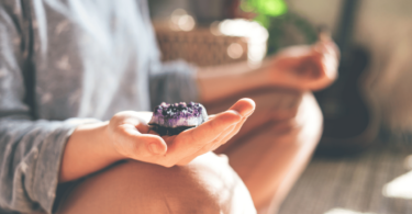 Uma mulher sentada está meditando com um cristal de quartzo na sua mão direita.