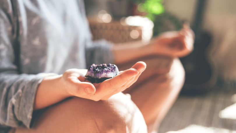 Uma mulher sentada está meditando com um cristal de quartzo na sua mão direita.