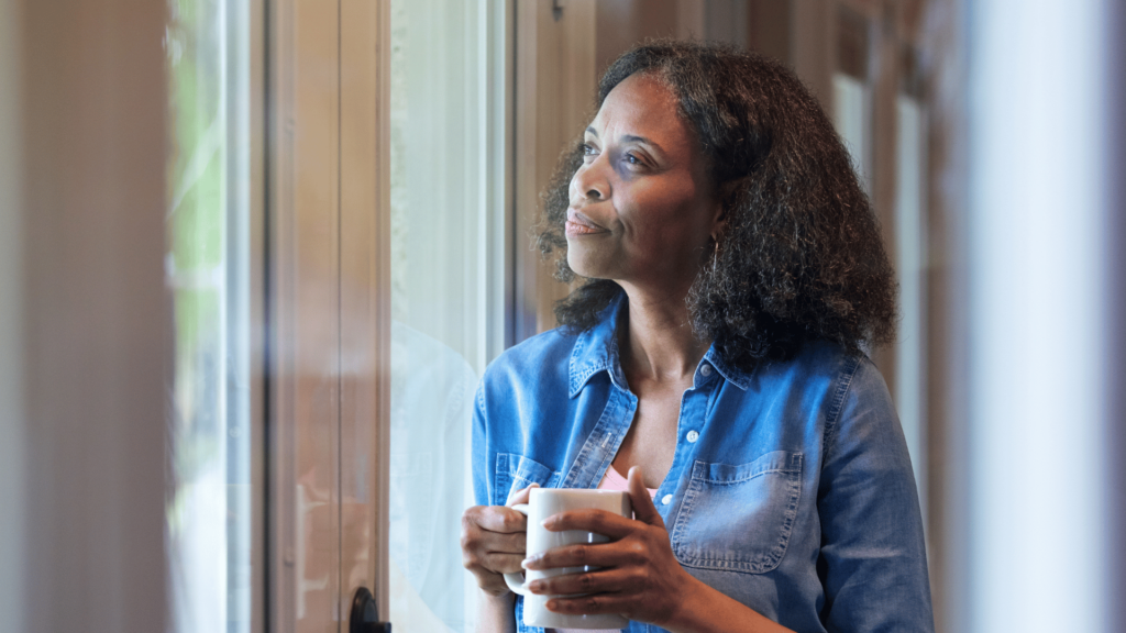 Uma mulher negra com uma feição reflexiva está olhando pela janela. 