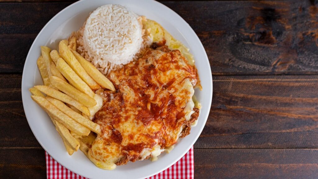 Imagem de um prato feito, composto por arroz, batata frita, frango à parmegiana.
