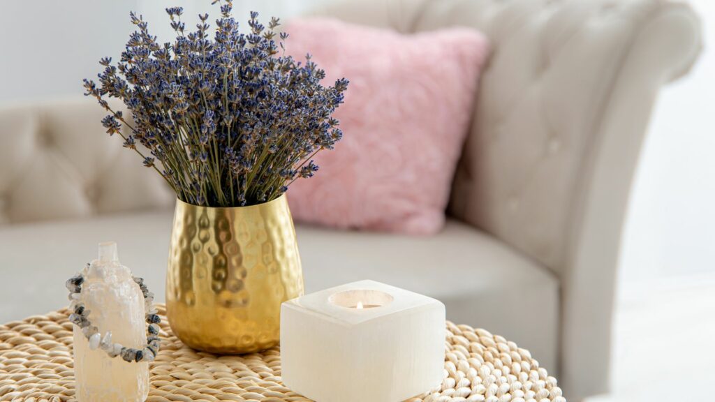 Imagem da pedra selenita como parte decoradora de uma sala de estar. Ela está disposta em uma mesa, ao lado de um vaso de lavanda e uma vela branca
