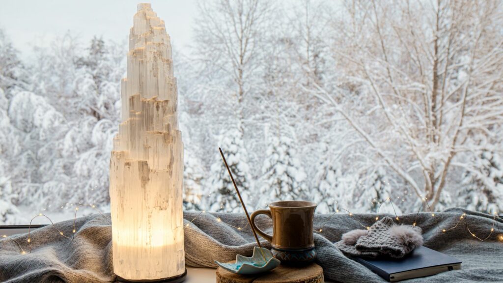 Imagem de uma grande pedra de selenita sobre uma mesa. Ao lado um incenso e um xícara de café para serem usados em um ritual.
