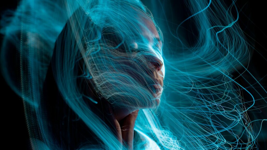 Imagem de uma mulher com cabelo azul e olhos azuis, envolta de fios energéticos iluminados e coloridos, simbolizando a matrix.
