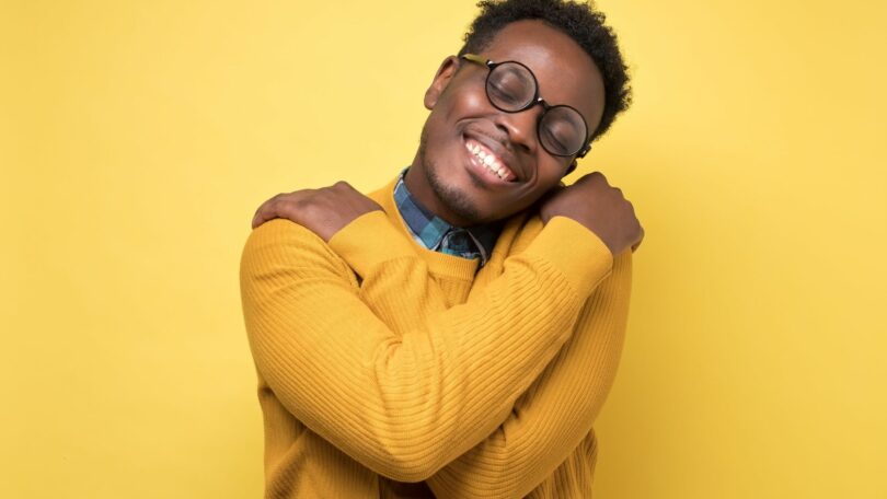 Imagem de um homem afro-americano se abraçando, trazedo o conceito de amor próprio e alta autoestima.