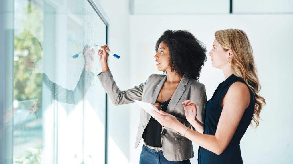 Imagem de duas mulheres traçando um plano para desenvolvimento humano em empresas para ajudar com a questão da saúde mental no trabalho.
