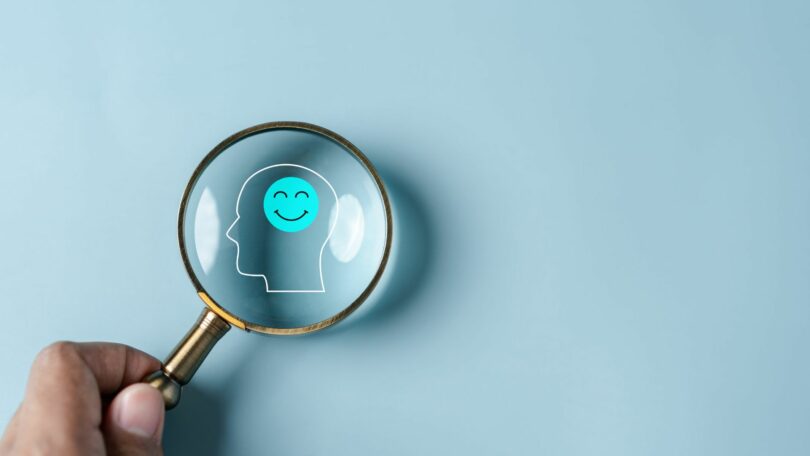 Imagem de fundo azul claro e em destaque uma lupa focando no cérebro humano, simbolizando sinal de saúde mental e pensamento positivo.