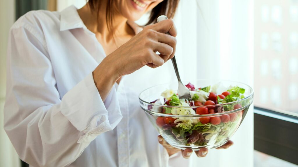 Imagem de uma mulher feliz, segurando um bowl de salada em suas mãos, trazendo o conceito de comer saudável.
