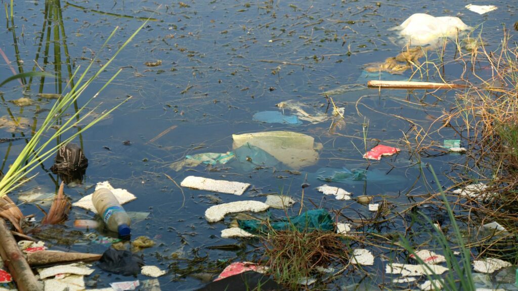 Imagem de um rio poluído e cheio de garrafas e pláticos.
