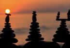 Imagem de 3 figuras feitas em pedra e ao fundo um lindo pôr do sol. A imagem traz o conceito de vida equilibrada e filosofia de vida.