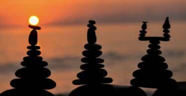 Imagem de 3 figuras feitas em pedra e ao fundo um lindo pôr do sol. A imagem traz o conceito de vida equilibrada e filosofia de vida.