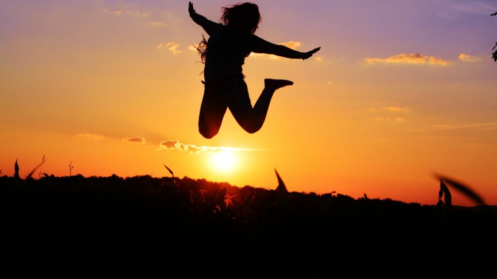 Imagem de uma mulher pulando na frente do pôr do sol, trazendo o conceito de renascimento para a vida.
