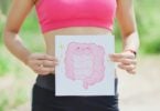 Imagem de uma mulher segurando uma placa com o desenho de um intestino. A foto traz o conceito da síndrome do intestino irritável.