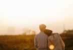 Imagem de um casal, homem e mulher, sentados olhando para o pôr do sol. Ela está com a cabeça encostada no ombro dele.