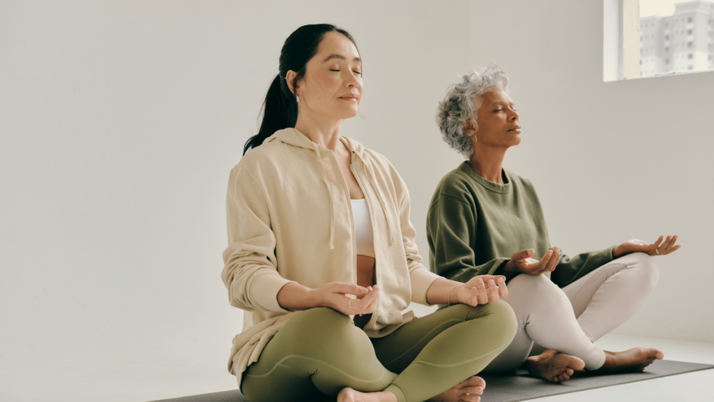 Duas mulheres estão meditando lado a lado em um ambiente fechado.