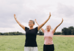 Imagem de duas mulheres, por volta dos 50 ou 60 anos, praticando Tai Chi ao ar livre em um parque.