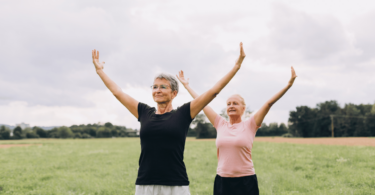 Imagem de duas mulheres, por volta dos 50 ou 60 anos, praticando Tai Chi ao ar livre em um parque.