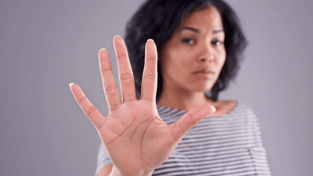 Uma mulher com uma expressão brava no rosto e a mão levantada está fazendo um sinal de "pare" com a mão direita.
