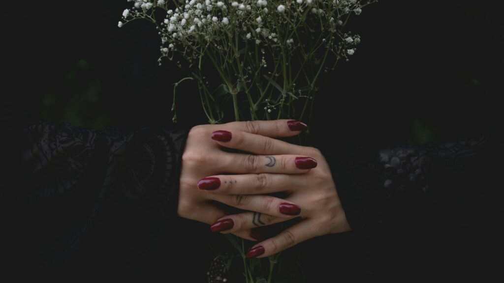 Imagem de fundo preto e em destaque as mãos de uma mulher com as unhas pintadas na cor vermelho, segurando um buquê de Gypsophila na cor branco.
