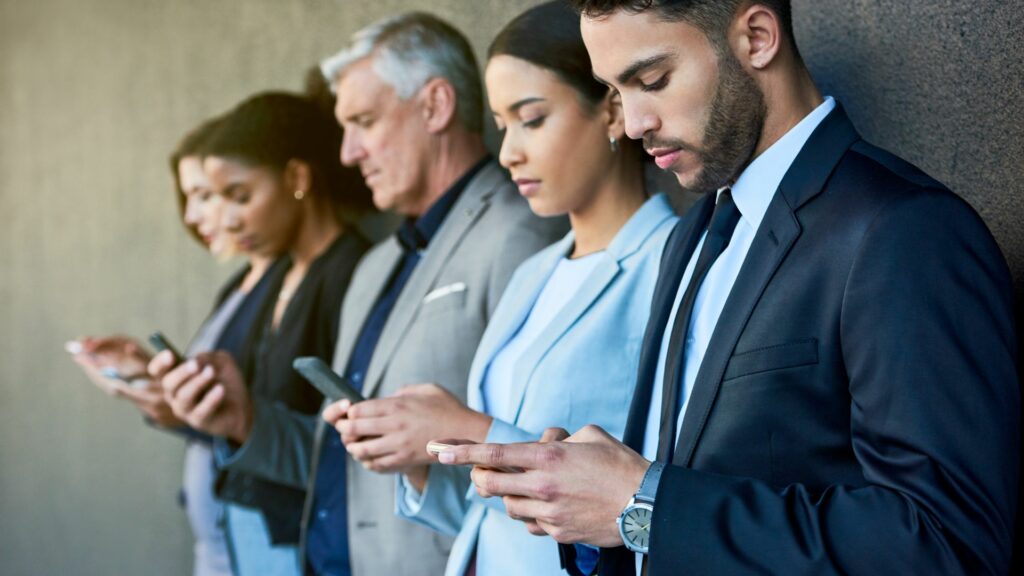 Imagem de várias pessoas, de várias idades, homens e mulheres com os seus celulares em mãos acessando às redes e usando as novas tecnologias.
