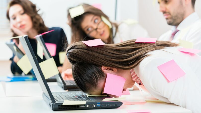Imagem de um grupo de pessoas trabalhando. Todas estão com um semblante de esgotamento, olhando para a frente do computador. A foto traz o conceito da síndrome de Boreout.