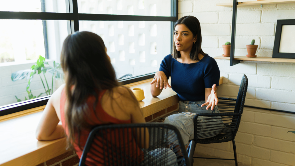 Duas mulheres estão sentadas uma de frente para a outra e estão conversando.