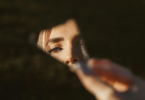 Uma mulher segura um fragmento de um espelho, o qual reflete uma parte do seu rosto.
