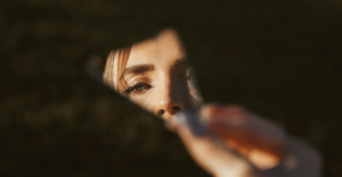 Uma mulher segura um fragmento de um espelho, o qual reflete uma parte do seu rosto.