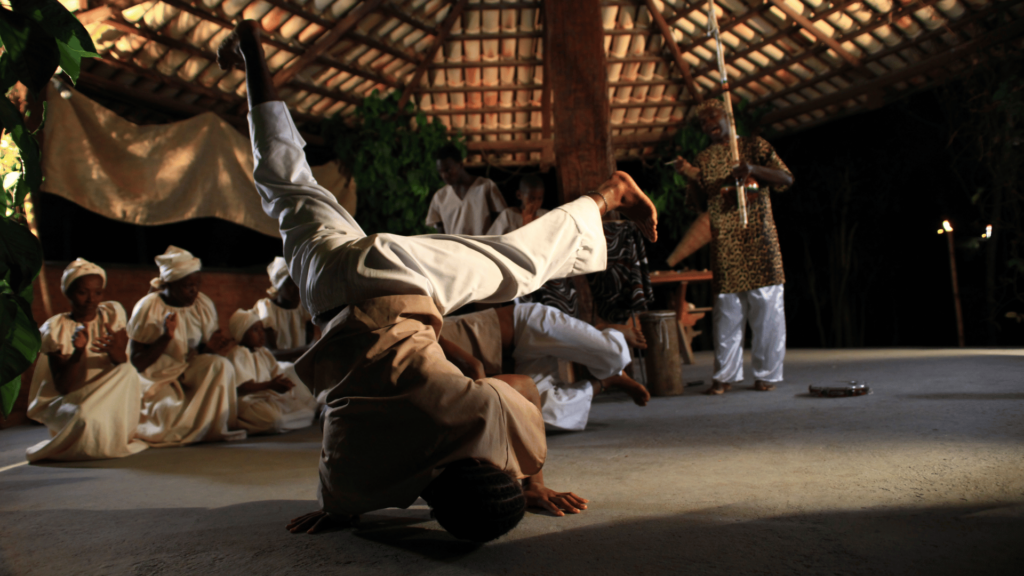 Um homem está fazendo capoeira na frente do seu grupo ou comunidade.