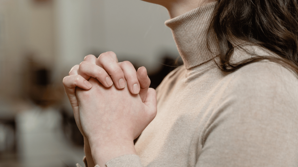 Uma mulher está segurando uma mão na outra em forma de oração, indicando esperança ou fé.