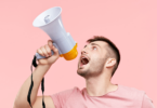 Um homem jovem está segurando e gritando em um megafone.
