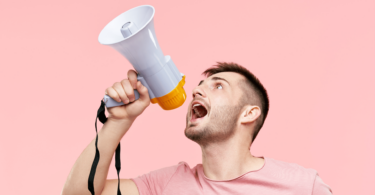 Um homem jovem está segurando e gritando em um megafone.