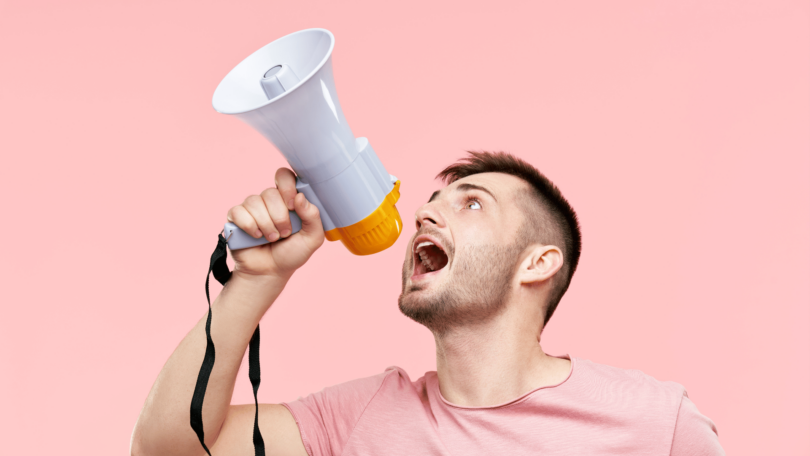 Um homem jovem está segurando e gritando em um megafone.