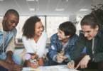 Um grupo de quatro estudantes faz um trabalho em conjunto. Eles sorriem um para o outro.