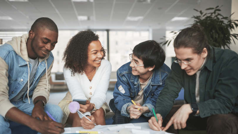 Um grupo de quatro estudantes faz um trabalho em conjunto. Eles sorriem um para o outro.