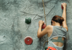 Uma mulher está fazendo escalada. Ela se segura nos suportes e sobe, indicando persistência, coragem e força.