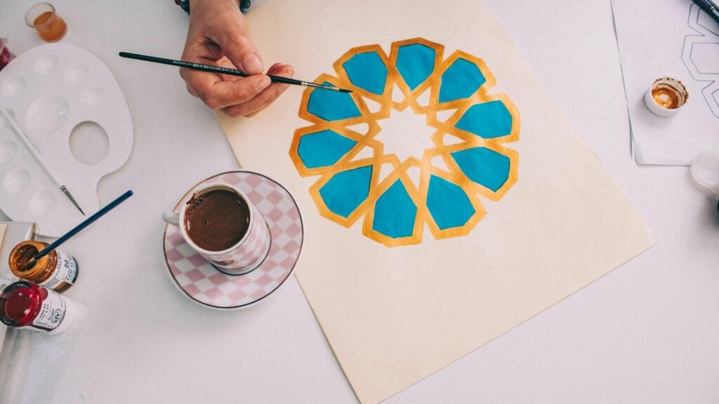 Imagem de um artista pintando uma linda mandala disposta sobre uma mesa.
