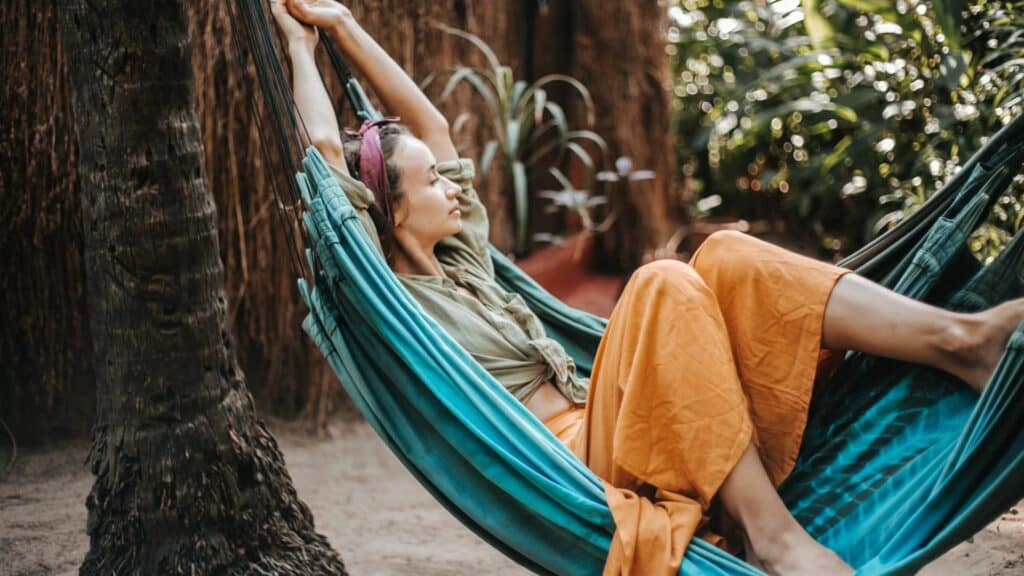Imagem de uma mulher deitada sobre uma rede na cor azul. Ela está descansando e vivendo uma realidade fora das redes sociais.